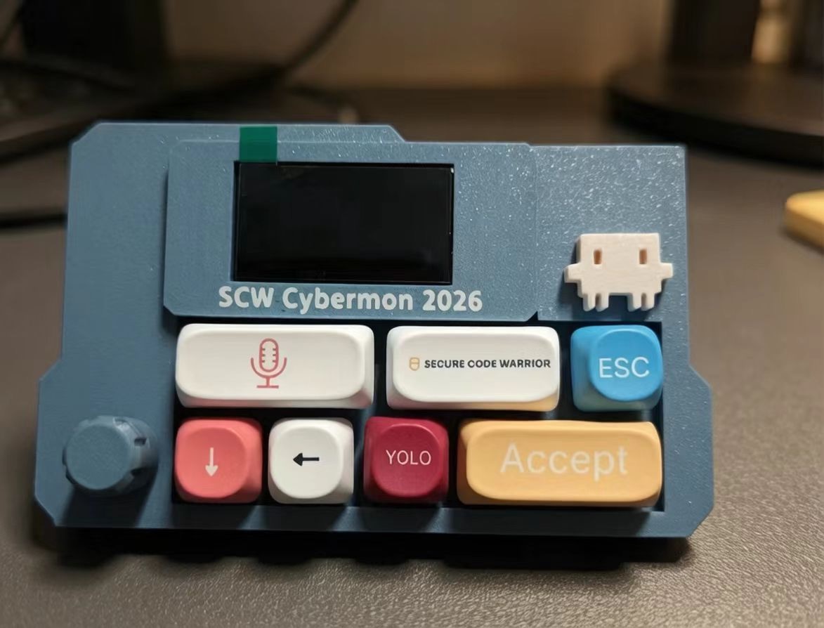 A co-branded VibeKeys Max made for an event: a blue case printed with "SCW Cybermon 2026", a custom Secure Code Warrior keycap, and keys for voice, ESC, YOLO and Accept